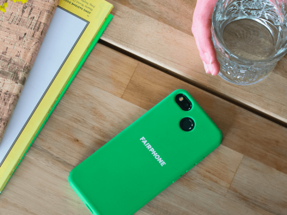 Bright green Fairphone lying next to office supplies on a wooden desk