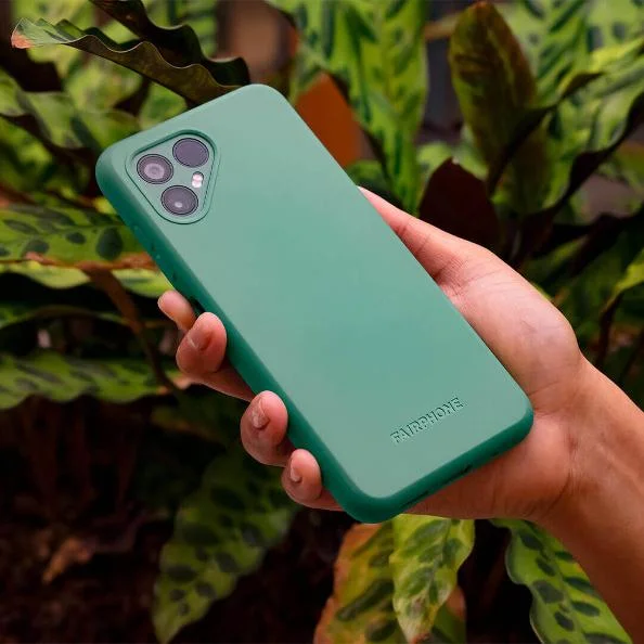 Hand holding a Fairphone with a vibrant green case in a natural setting, featuring a triple-camera setup highlighted against lush indoor plants, emphasizing the eco-friendly aspect of the brand.