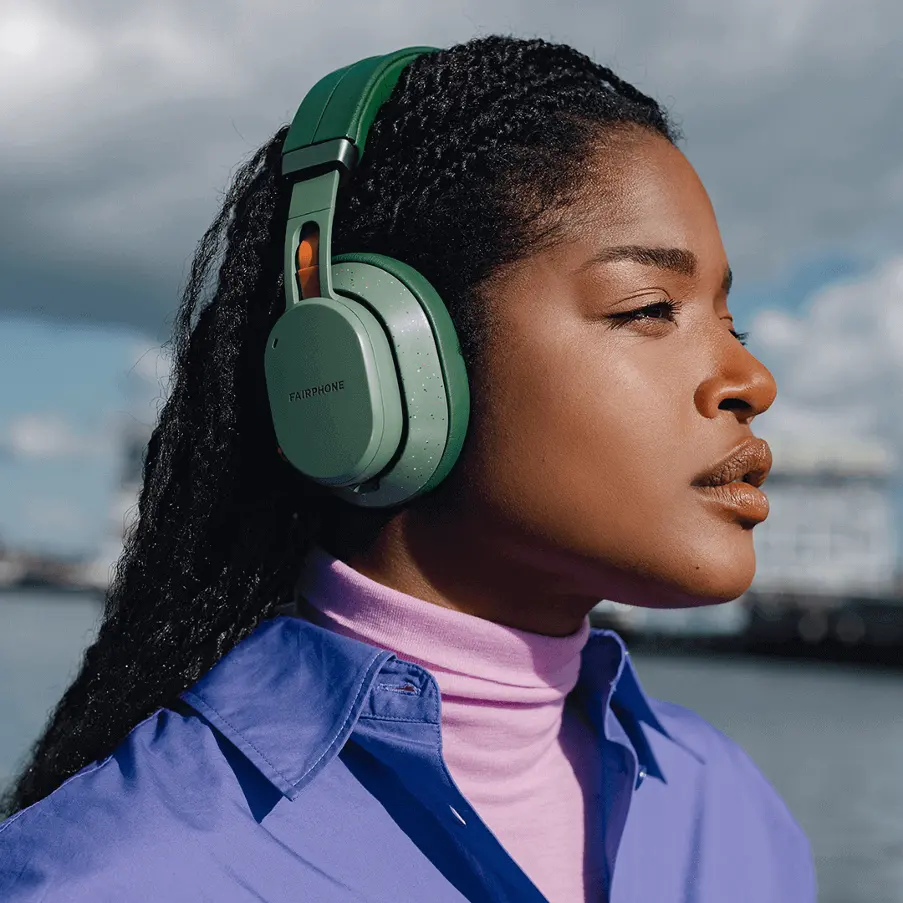 Side profile of a woman wearing green Fairphone wireless headphones outdoors.